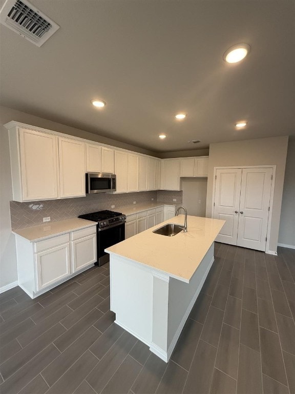 kitchen with white cabinets, a center island with sink, sink, and appliances with stainless steel finishes