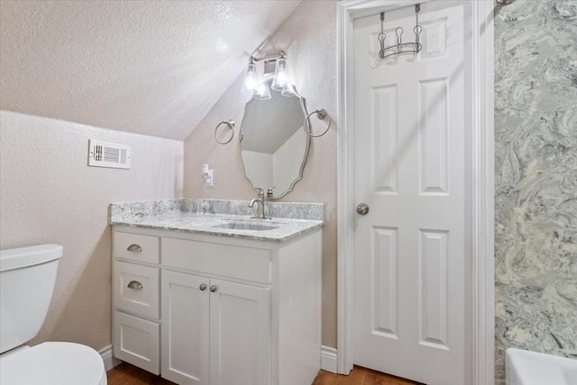 bathroom with hardwood / wood-style floors, vanity, vaulted ceiling, toilet, and a textured ceiling