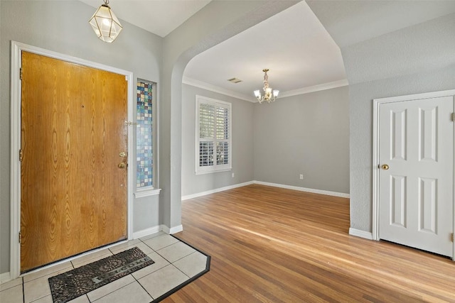 foyer entrance featuring wood-type flooring, ornamental molding, and an inviting chandelier