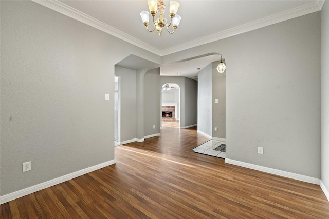 spare room featuring a notable chandelier, a fireplace, crown molding, and dark wood-type flooring