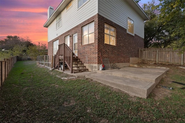 property exterior at dusk with a lawn and a patio