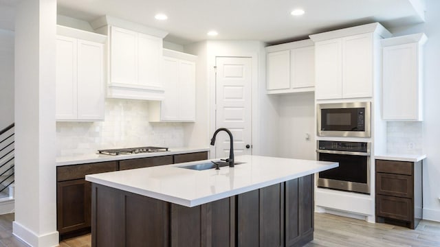 kitchen with appliances with stainless steel finishes, light wood-type flooring, backsplash, and a sink