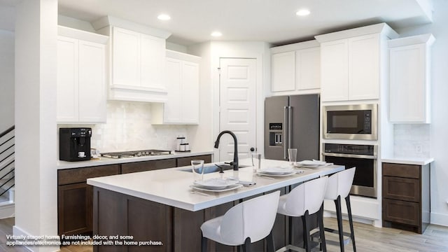 kitchen with tasteful backsplash, light wood-style flooring, appliances with stainless steel finishes, a sink, and a center island with sink
