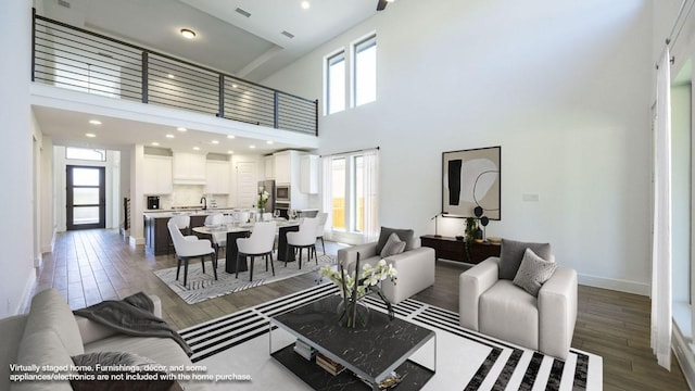 living area featuring recessed lighting, visible vents, baseboards, a towering ceiling, and wood finished floors