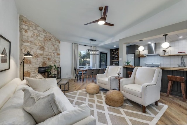 living room with a stone fireplace, ceiling fan, light hardwood / wood-style flooring, and vaulted ceiling