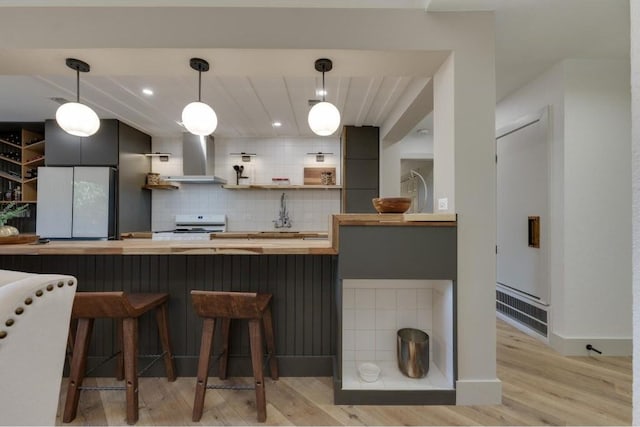 kitchen featuring wall chimney range hood, a kitchen breakfast bar, decorative light fixtures, white stove, and light wood-type flooring