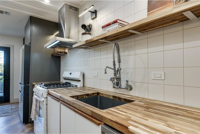 kitchen with white cabinets, hardwood / wood-style flooring, decorative backsplash, white gas stove, and butcher block counters