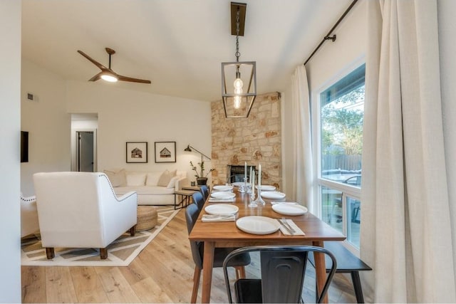 dining space with ceiling fan, lofted ceiling, a fireplace, and light hardwood / wood-style flooring