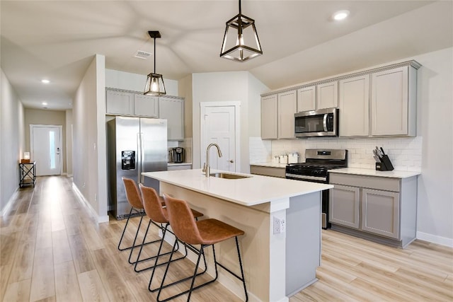 kitchen featuring light wood-type flooring, gray cabinetry, stainless steel appliances, sink, and decorative light fixtures