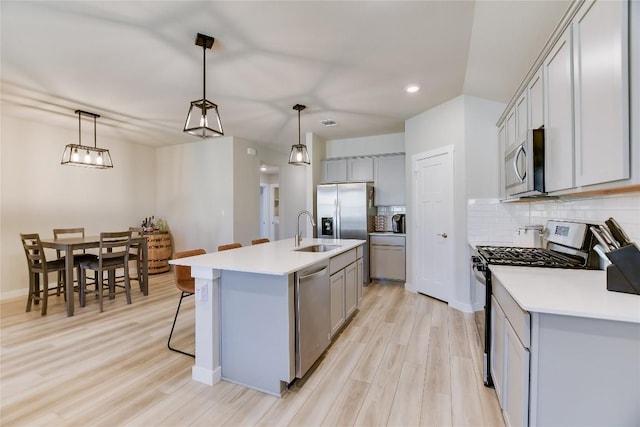 kitchen featuring an island with sink, light hardwood / wood-style floors, decorative light fixtures, and appliances with stainless steel finishes