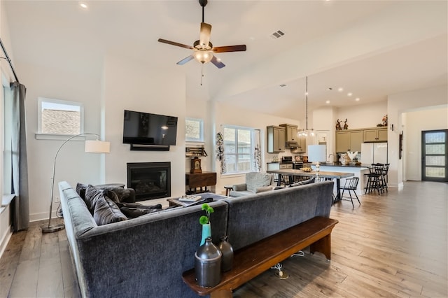 living room featuring ceiling fan, light wood-type flooring, and a towering ceiling