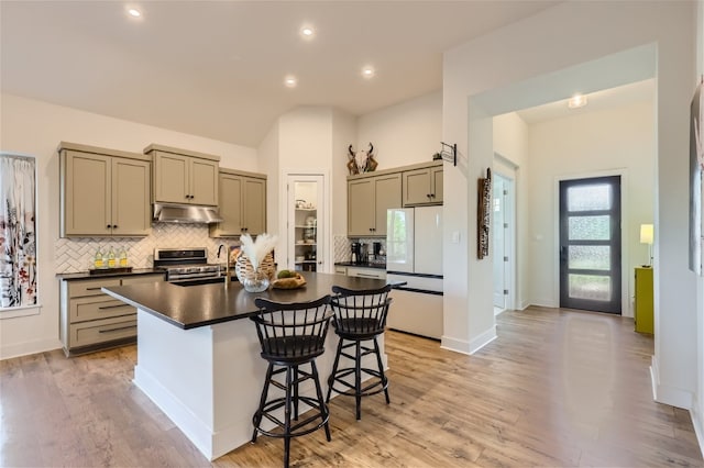 kitchen featuring a center island with sink, a kitchen breakfast bar, light wood-type flooring, stainless steel range, and white fridge