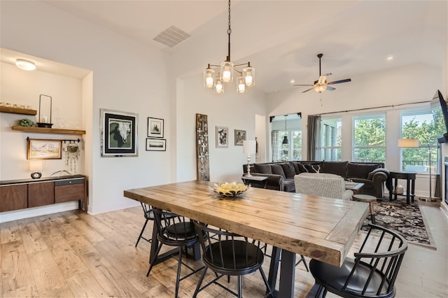 dining room with ceiling fan with notable chandelier, light wood-type flooring, and high vaulted ceiling