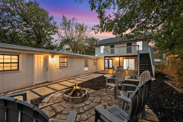 back house at dusk featuring a patio area, a fire pit, and a balcony