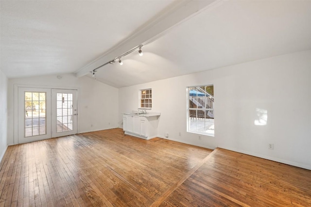 unfurnished living room with lofted ceiling with beams, french doors, light wood-style flooring, baseboards, and rail lighting