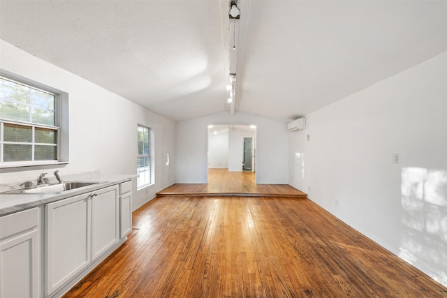 unfurnished living room with vaulted ceiling, a wall unit AC, sink, and light hardwood / wood-style flooring