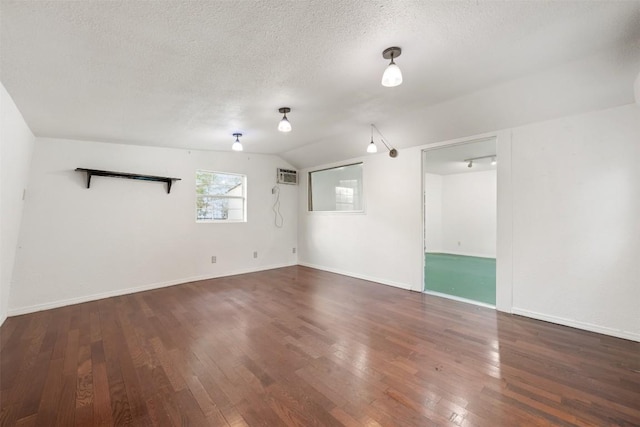 spare room with lofted ceiling, an AC wall unit, baseboards, a textured ceiling, and hardwood / wood-style flooring