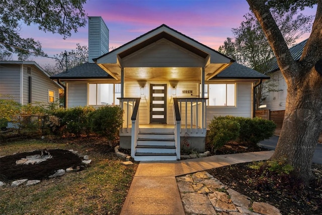 bungalow-style house with a chimney, fence, a porch, and a shingled roof