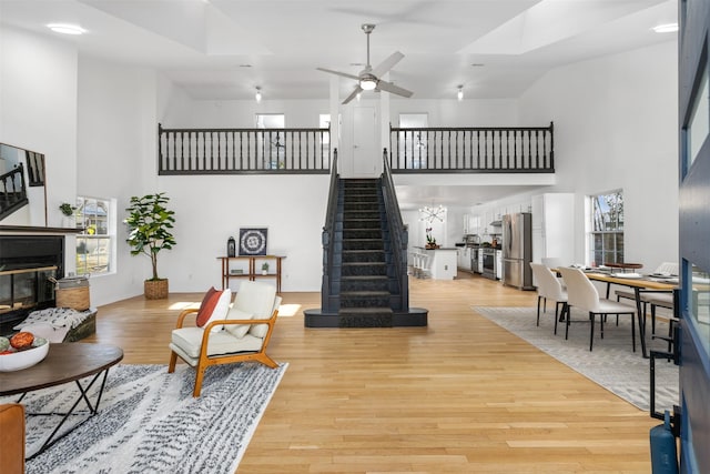 living room featuring ceiling fan, a towering ceiling, and light wood-type flooring