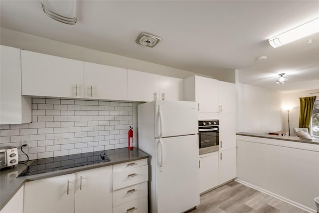 kitchen featuring stainless steel oven, decorative backsplash, white fridge, and white cabinetry