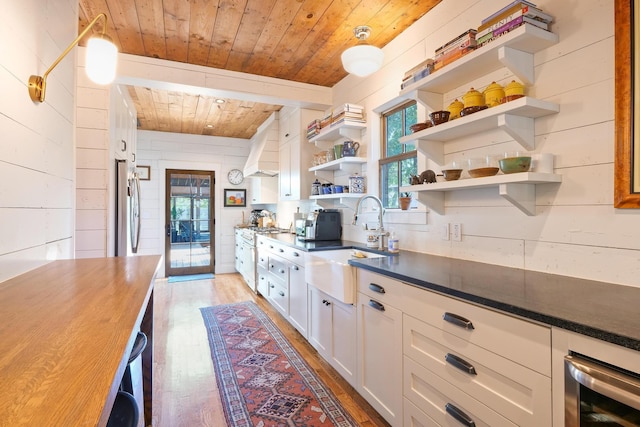 kitchen with sink, wood ceiling, white cabinets, light wood-type flooring, and wood walls