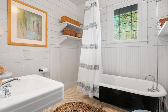 bathroom featuring wood walls, a freestanding tub, a shower with shower curtain, and a sink