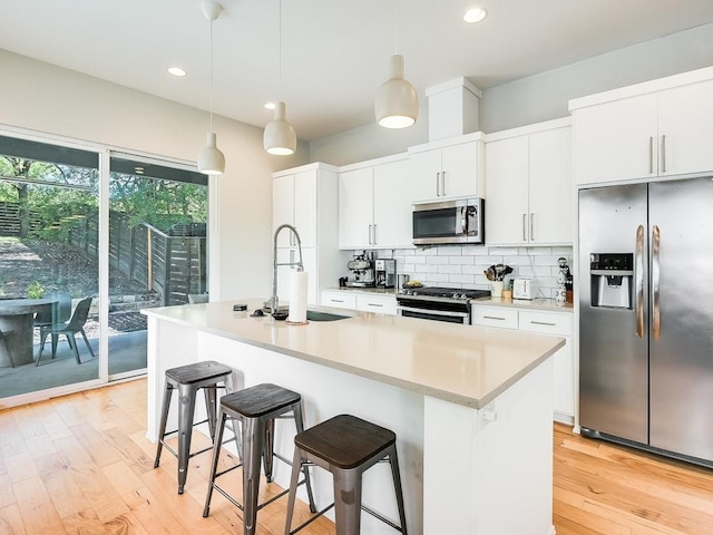 kitchen featuring appliances with stainless steel finishes, decorative light fixtures, and an island with sink