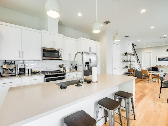 kitchen with light wood-type flooring, decorative light fixtures, a kitchen bar, white cabinetry, and stainless steel appliances