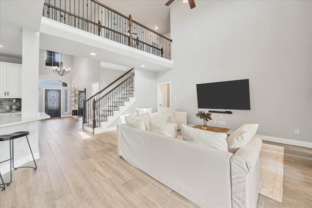 living room with light wood-type flooring, ceiling fan with notable chandelier, and a high ceiling