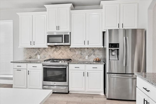 kitchen with light stone countertops, white cabinets, appliances with stainless steel finishes, decorative backsplash, and light hardwood / wood-style flooring