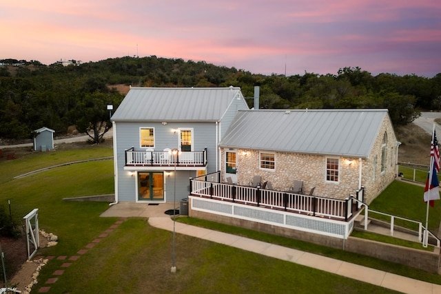 back house at dusk with a balcony and a yard