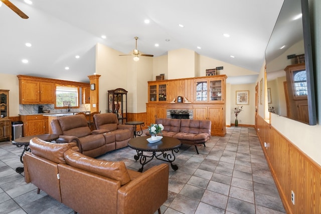 living room featuring ceiling fan, a fireplace, high vaulted ceiling, and wooden walls