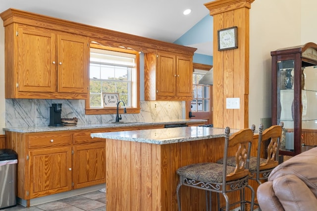 kitchen featuring lofted ceiling, backsplash, a kitchen breakfast bar, sink, and light stone counters