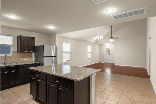 kitchen with light tile patterned flooring, sink, vaulted ceiling, stainless steel fridge, and a kitchen island