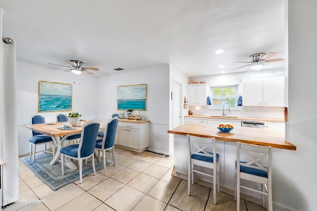 kitchen with a kitchen bar, sink, butcher block countertops, white cabinetry, and light tile patterned floors