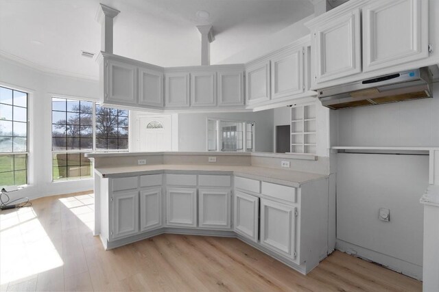 kitchen with kitchen peninsula, crown molding, extractor fan, light hardwood / wood-style floors, and white cabinets