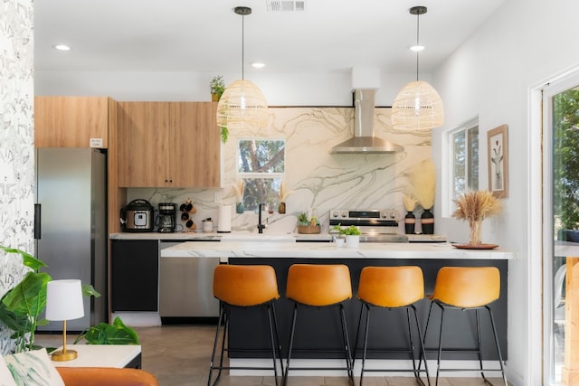 kitchen featuring appliances with stainless steel finishes, decorative backsplash, a kitchen bar, and wall chimney range hood