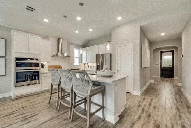 kitchen with white cabinetry, wall chimney exhaust hood, light hardwood / wood-style floors, a kitchen island, and appliances with stainless steel finishes