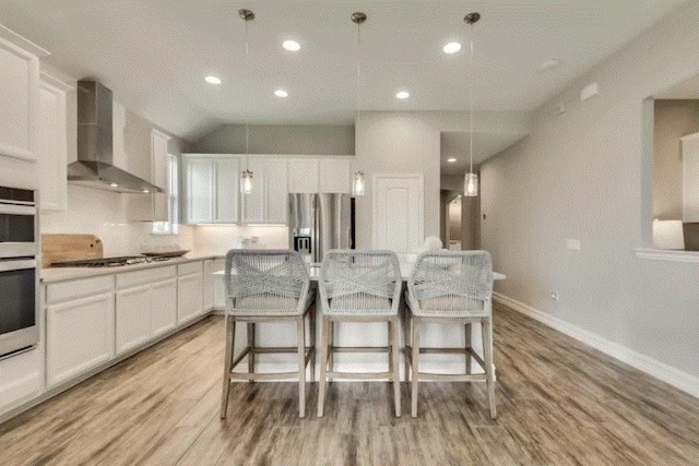 kitchen with decorative light fixtures, stainless steel appliances, white cabinetry, and wall chimney range hood