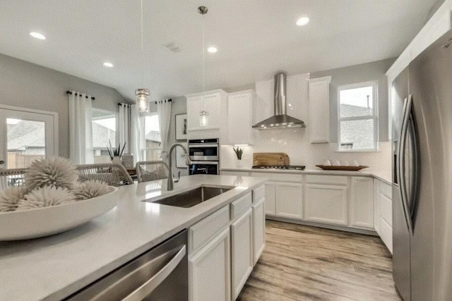 kitchen featuring white cabinetry, sink, wall chimney exhaust hood, light hardwood / wood-style flooring, and appliances with stainless steel finishes