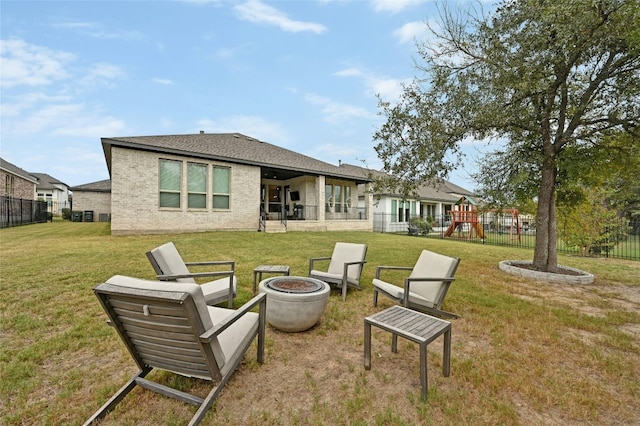 rear view of property featuring a yard, a playground, and an outdoor fire pit