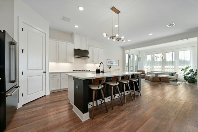 kitchen featuring pendant lighting, a kitchen island with sink, white cabinets, stainless steel refrigerator, and a chandelier