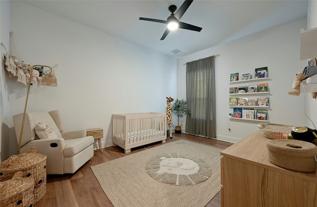 bedroom with hardwood / wood-style floors, ceiling fan, and a crib