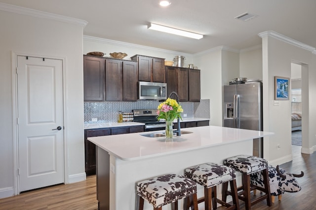 kitchen with stainless steel appliances, crown molding, light hardwood / wood-style floors, and an island with sink