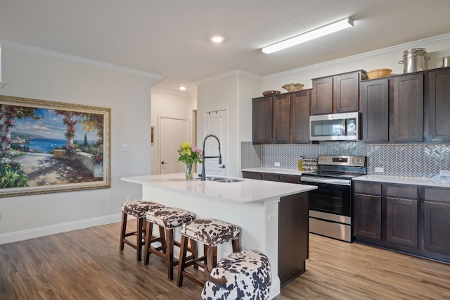 kitchen featuring stainless steel appliances, a kitchen island with sink, crown molding, sink, and light hardwood / wood-style floors