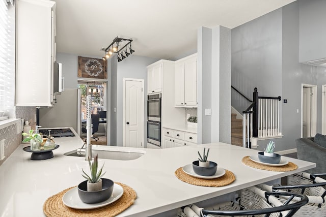 kitchen featuring a kitchen bar, kitchen peninsula, refrigerator, double oven, and white cabinetry