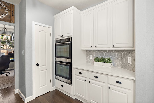 kitchen with white cabinets, dark wood-type flooring, double oven, and tasteful backsplash