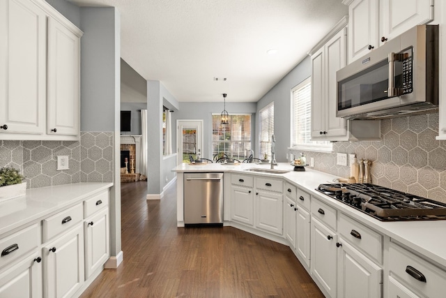 kitchen featuring appliances with stainless steel finishes, a brick fireplace, dark hardwood / wood-style floors, white cabinetry, and hanging light fixtures