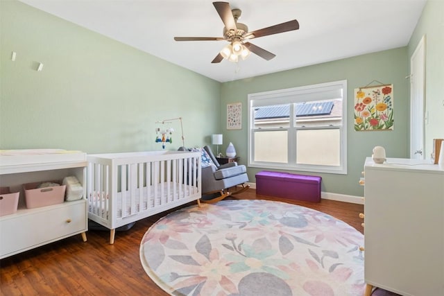 bedroom featuring a nursery area, ceiling fan, and dark wood-type flooring