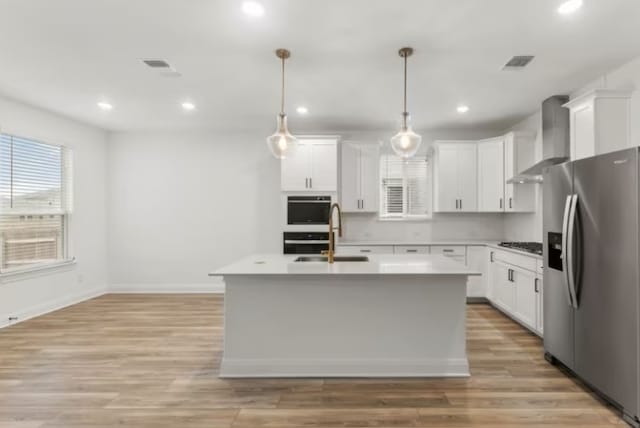 kitchen featuring white cabinets, an island with sink, wall chimney range hood, and appliances with stainless steel finishes